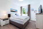 Schlafzimmer mit Doppelbett, Kommode und TV - Aparthotel Ostseeallee 4-34 - Top-Hundeurlaub