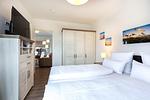 Schlafzimmer mit Boxspringbett, Kleiderschrank, TV und Blick zum Wohn-/Essbereich - Aparthotel Ostseeallee 4-38 - Top-Hundeurlaub