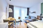 Wohn-Ess-Schlafbereich mit Sofa, Esstisch, Sitzgelegenheit und Doppelbett sowie Zugang zum Balkon - Deichhäuser Anna Küste 4-22 - Top-Hundeurlaub