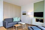Wohn/ Essbereich mit Couch, Tisch und Fernseher - Aparthotel Anna Düne 1-23 - Top-Hundeurlaub