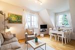 The living room features a cozy sofa, a TV, and an elegant dining table. Large windows let in plenty of sunlight. - Strandleben 10 - Louis Douzette - Top-Hundeurlaub