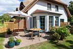 Reetgedecktes Haus mit Terrasse, Sonnenschirm, Sitzgruppe und blühenden Büschen. - Boddenblick 1 - Top-Hundeurlaub
